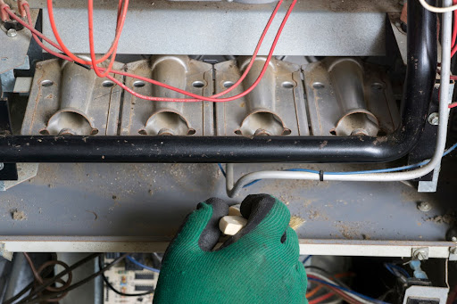 Technician cleaning a burner area of a natural gas furnace.