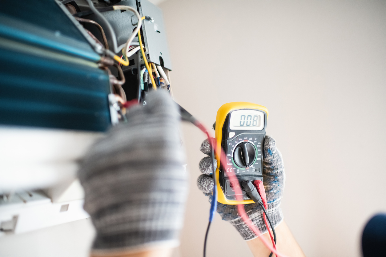Technician using a multimeter to service an indoor air‑conditioner unit.